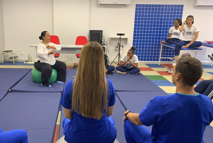 A physiotherapist sits on an exercise ball in front of a class