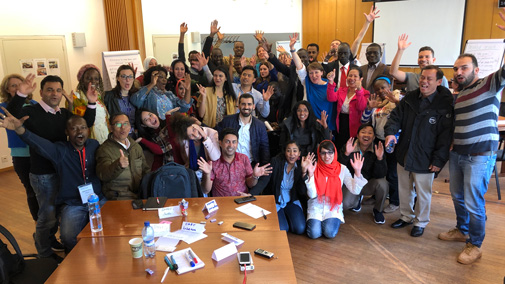 Workshop participants raise their hands and smile during the session
