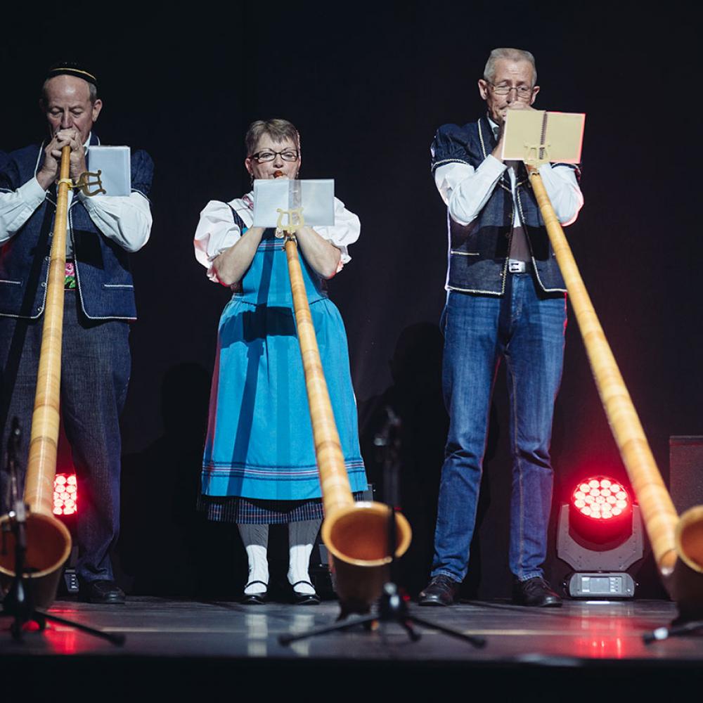 Three people on stage playing alpine horns